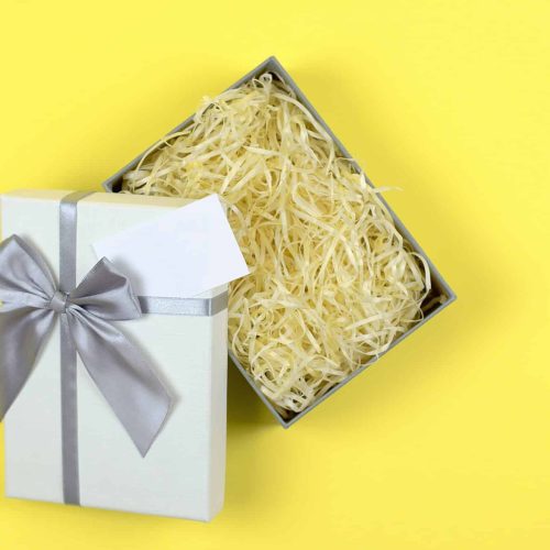 Gift box with filler on a yellow background for product advertising. Open gift box mockup, flat lay